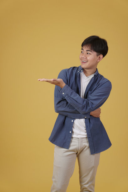 快乐的英俊年轻亚洲男人穿着休闲装，在黄色背景的复制空间上张开手掌图片下载