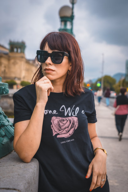 城市生活方式。一个年轻的黑发女子，戴着墨镜，穿着黑色短裤，黑色t恤和白色运动鞋。在城市的河边沉思图片下载