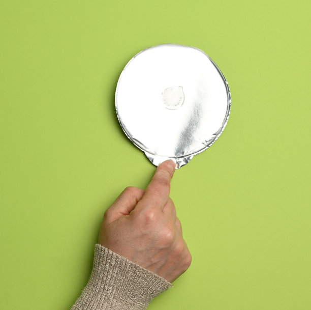 绿色背景上的塑料酸奶罐的圆形铝薄盖图片下载