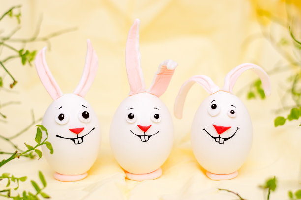 复活节快乐的概念。富有创意的复活节兔子，蛋上画着有趣的面孔。黄色背景,鲜花。图片下载