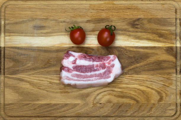 一块猪肉放在厨房的板子上，两个红番茄。图片下载