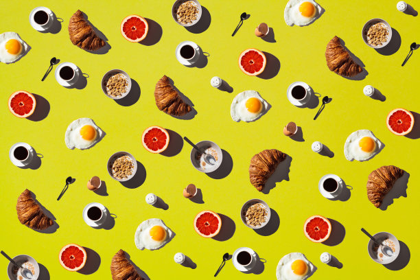 早餐食物平放。煎蛋，玉米片碗，羊角面包，葡萄柚和咖啡在黄色的背景。图片下载