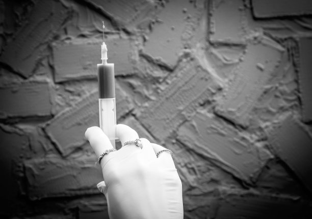 黑白照片，医生的手戴着手套，戴着珠宝，拿着一个注射器，针头向上，在蓝色的背景图片下载