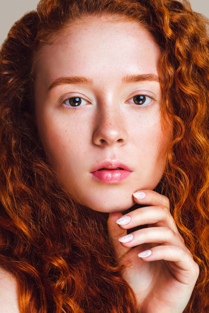 一个红头发女孩的特写，卷头发，小雀斑和棕色眼睛。美丽的模特看着镜头。这张修过的照片是在摄影棚里拍的。皮肤没有化妆图片下载