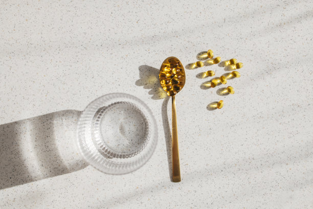 维生素D药丸在茶匙中，放在桌子上，旁边是一杯水(高角度照片)图片下载