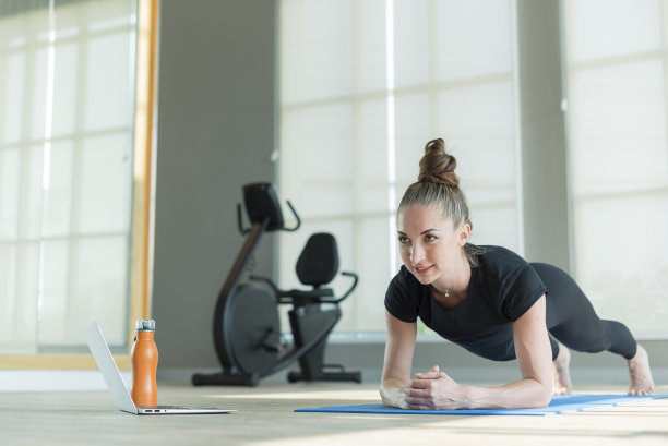 年轻强壮的健身女性在瑜伽垫上做平板支撑运动，并在健身房的笔记本电脑上在线学习锻炼课程图片下载
