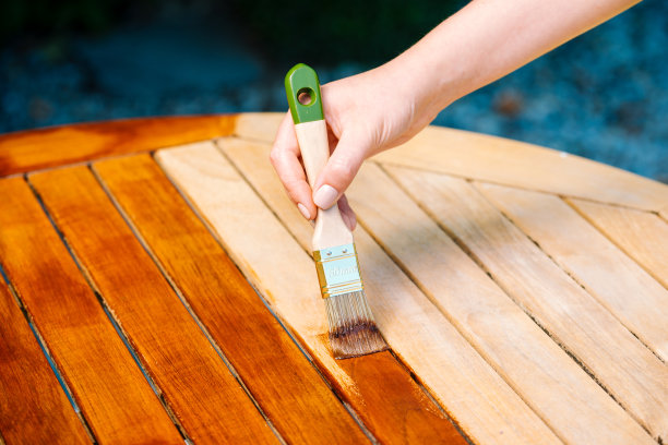 手拿刷子应用清漆油漆在一个木制花园桌子绘画和照顾木材与油图片下载