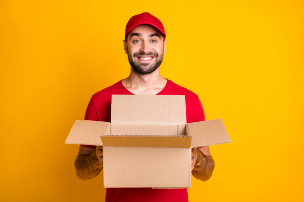 照片肖像滑稽的信使保持打开的箱子的财产包装微笑孤立在明亮的黄色背景图片下载