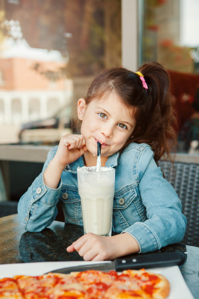 有趣的微笑的高加索学前班女孩喝奶昔与纸吸管在咖啡馆。孩子们在餐厅的露台上吃午餐，享受食物和饮料。快乐真实的童年生活方式。图片下载