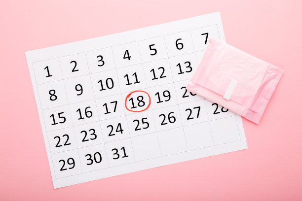 白色日历和卫生巾包在浅粉色的桌子背景上。柔和的颜色。特写镜头。月经周期。自顶向下的观点。图片下载