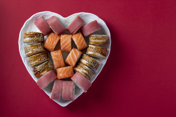 寿司:三文鱼、金枪鱼和鳗鱼，配以费城芝士心，红色背景。情人节食物概念。俯视图图片下载