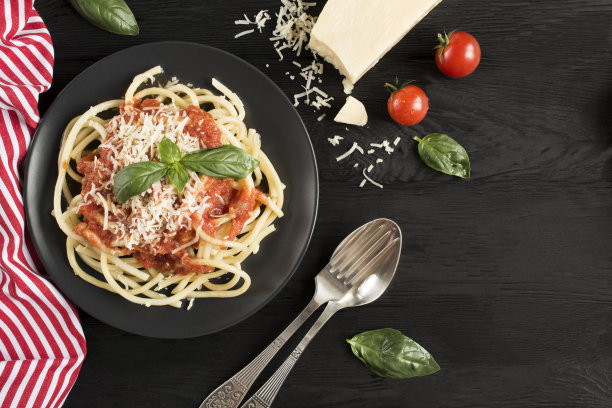 深色木色背景上的黑色盘子里有番茄酱和帕尔马干酪的意大利面食图片下载