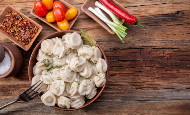 自制饺子，酸奶油和莳萝，放在一张老式木制桌子上，还有新鲜的西红柿、洋葱和香料图片下载