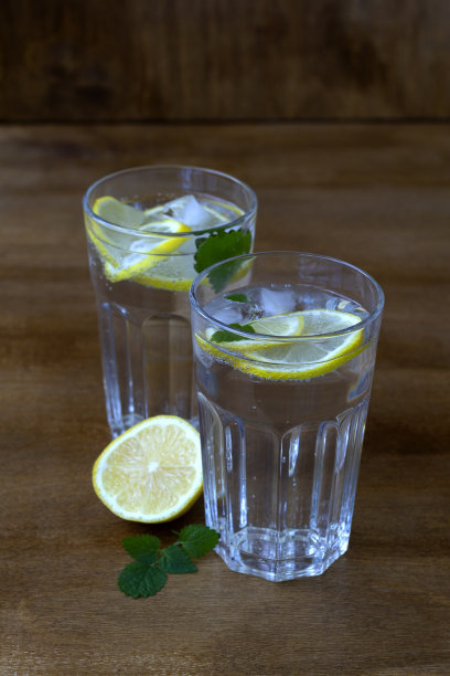 木桌上的莫吉托鸡尾酒。两杯柠檬水或莫吉托鸡尾酒加柠檬和薄荷。冷饮或水与冰在乡村木材背景。副本的空间。垂直的。夏季饮料。图片下载