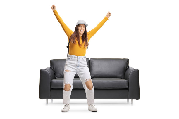 一个快乐的年轻女性从沙发上跳下来的全长肖像图片下载