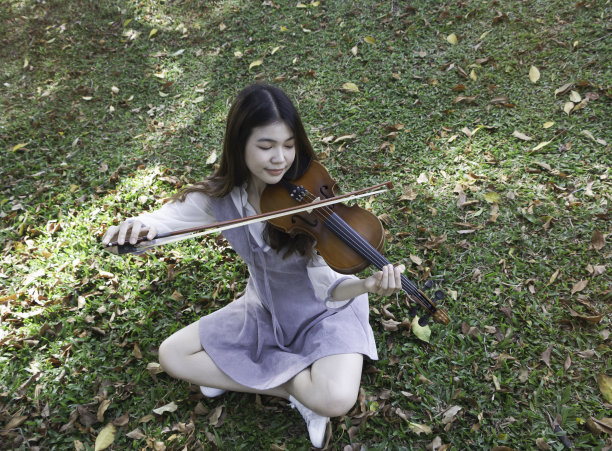年轻美丽的女士在公园拉小提琴图片下载