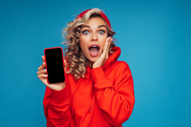 美丽的女人站在蓝色背景前拿着智能手机图片下载