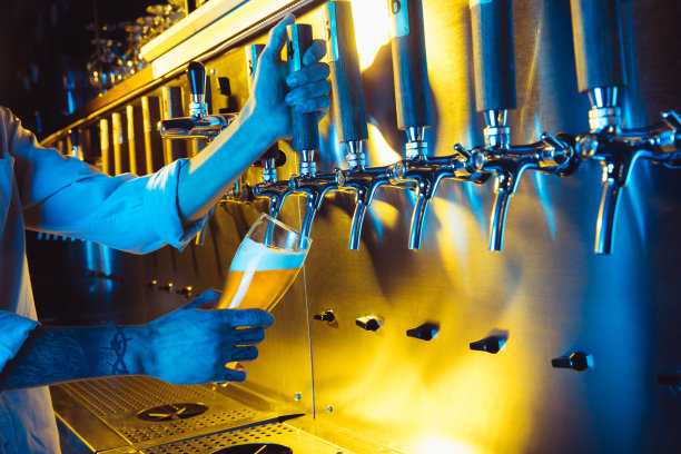 在霓虹灯下，调酒师将冰镇啤酒从龙头倒入玻璃杯。图片下载