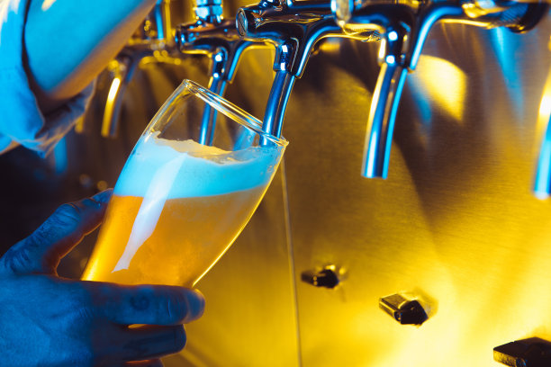 在霓虹灯下，调酒师将生啤酒从龙头倒入玻璃杯。图片下载