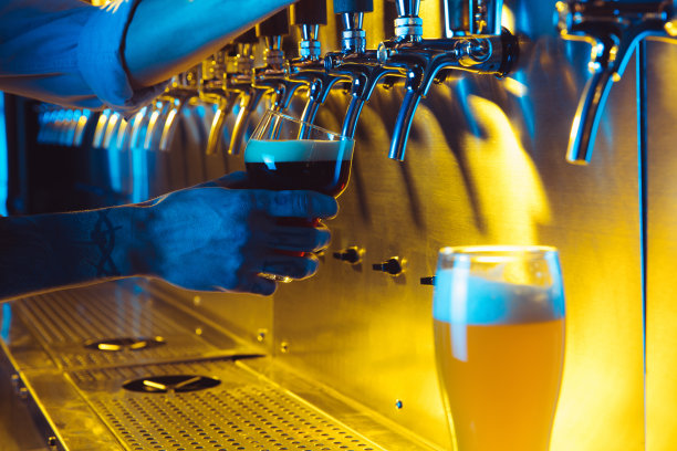 在霓虹灯的照耀下，酒吧招待将新鲜的黑啤酒从龙头倒入玻璃杯。图片下载