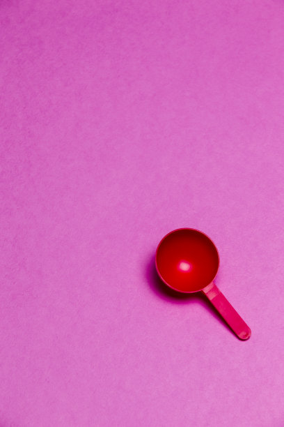 红色塑料圆形汤匙放置在彩色的粉红色背景。垂直的图像图片下载