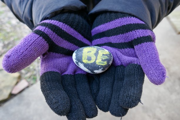 戴着黑色和紫色手套的人用BE的信息举着仁慈的石头图片下载
