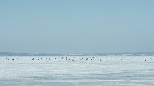 许多渔民冬天在冰冻的湖面上钓鱼在蓝天的背景。休闲活动的概念。空间的文本。图片下载