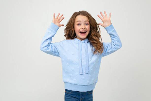 一个穿着蓝色连帽衫的迷人少女在浅灰色背景下开心地笑着，她的手掌放在面前图片下载