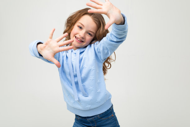 可爱的欧洲少女在一个蓝色帽衫显示十个手指在浅灰色的背景图片下载