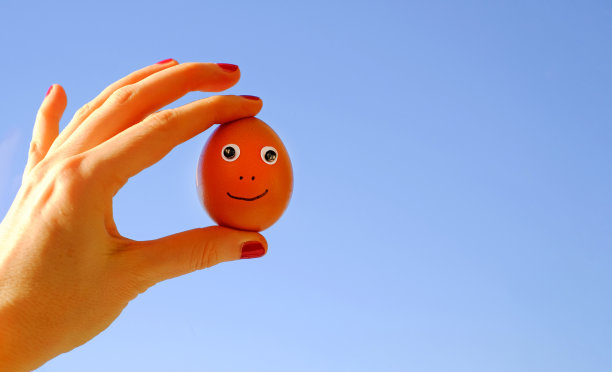 有趣的鸡蛋与眼睛在一个手在蓝天阳光的背景，复制空间图片下载