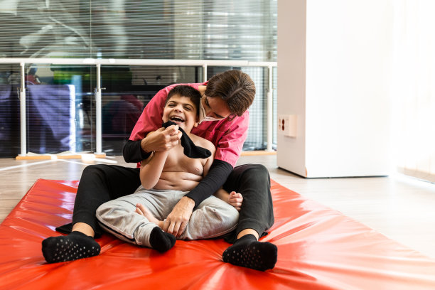 残疾儿童和理疗师在红色体操垫上做练习。大流行面具保护图片下载