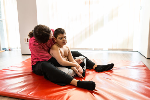 残疾儿童和理疗师在红色体操垫上做练习。大流行面具保护图片下载