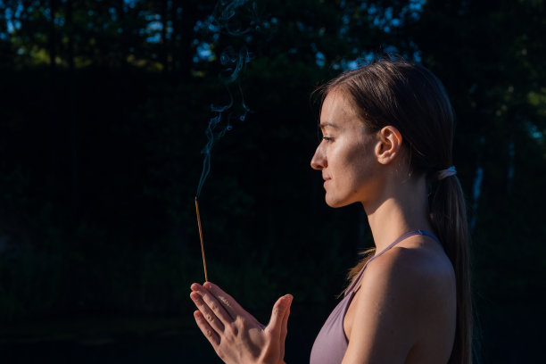 一个女人在户外做瑜伽冥想，手里拿着香薰棒，手掌合十礼图片下载