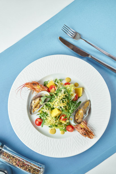 搭配海鲜、海螯虾、贻贝、芝麻菜和圣女果的开胃沙拉放在蓝色桌布上的白色盘子里图片下载