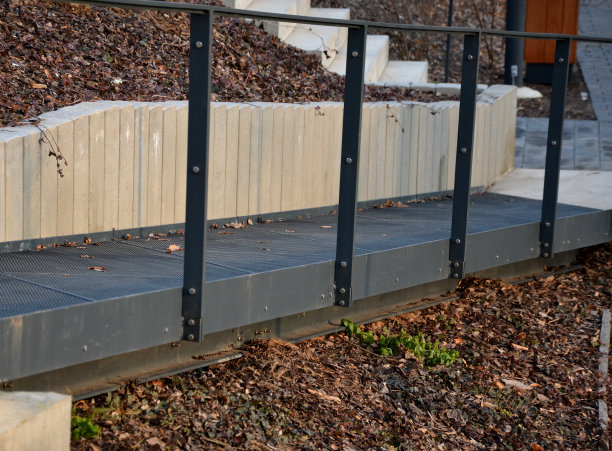 由金属格栅人行天桥或人行天桥制成的坡道。通往下坡的灰色混凝土护栏和专为轮椅而设的栏杆。城市公园的入口。图片下载