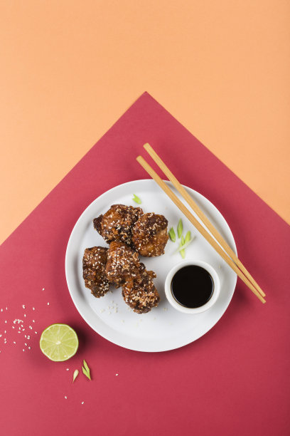 红烧鸡和芝麻放在一个平盘子里，配上酸橙、酱油和筷子，背景颜色鲜艳。图片下载