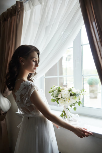 新娘的早晨。一个漂亮的女人正在为一场婚礼做准备，她有着自然的妆容和别致的发型。白色的睡衣和婚纱图片下载