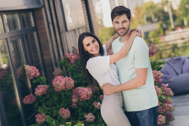 浪漫欢快的情侣拥抱的照片，看着相机，灿烂的微笑，穿着休闲衣服在花园公园外面图片下载