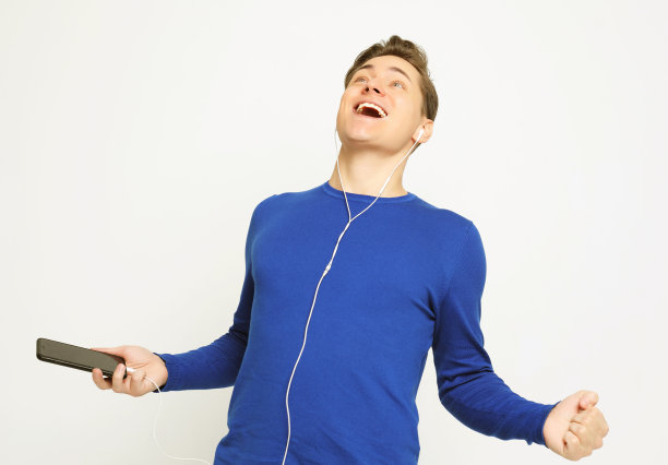 快乐的年轻时尚男子调整他的耳机和微笑，而站在白色的背景图片下载