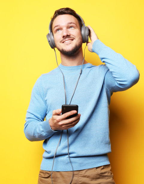 英俊的年轻人在黄色背景下听音乐图片下载