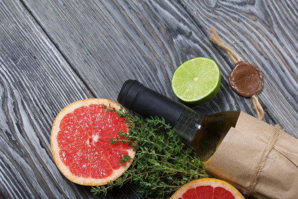酒精瓶。包裹在纸上。旁边放着百里香，半块酸橙和葡萄柚。松木板。图片下载