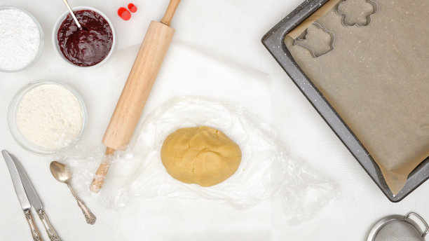 烘焙工艺，食品背景。酥饼曲奇饼面团，烤盘内衬羊皮纸，滚轴，饼干切刀和一些材料靠近图片下载