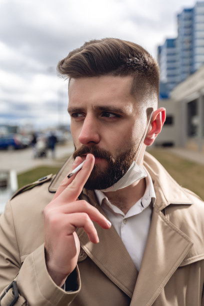 大街上的现代大胡子男人的肖像。生活理念与复制空间。穿着米色夹克和白衬衫的帅哥。他很累，下班后还带着医用口罩抽烟图片下载