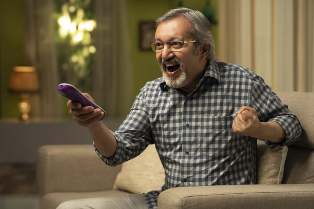 一个成熟的男人坐在沙发上看电视-库存照片图片下载