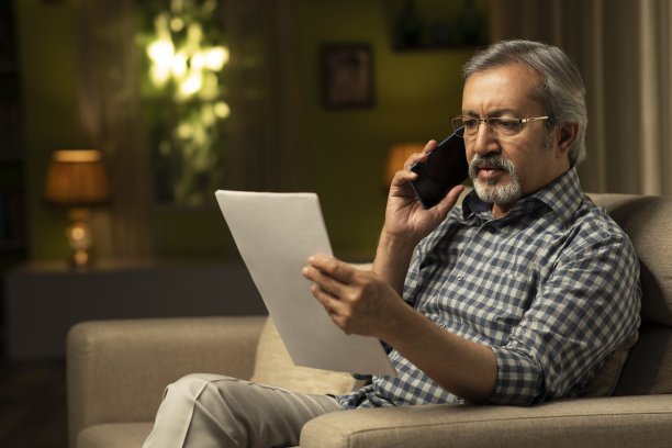 中年男人在家中沙发上阅读文件并打电话，库存照片图片下载