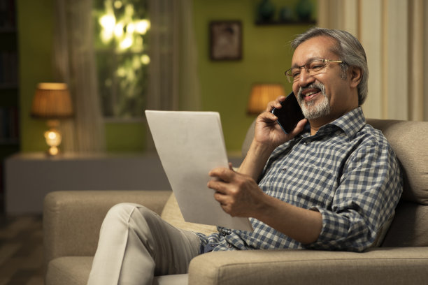 中年男人在家中沙发上阅读文件并打电话，库存照片图片下载