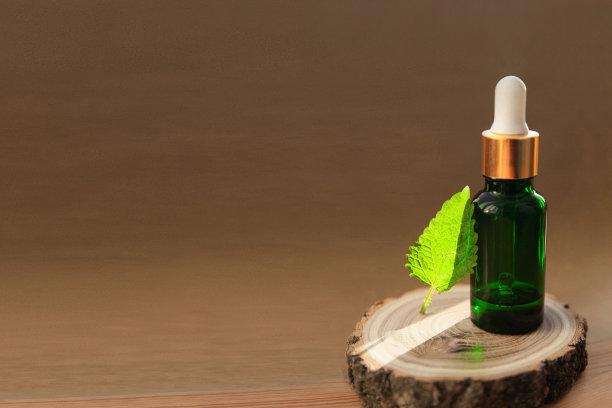 在阳光下的木片上放着一瓶绿色的玻璃薄荷油和一片新鲜的叶子图片下载