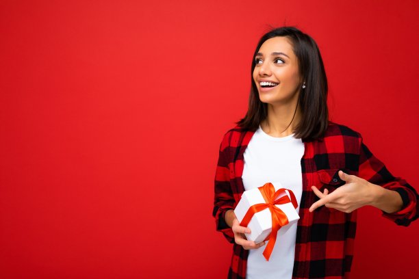 照片拍摄的相当积极的快乐惊喜年轻的黑发女人孤立在色彩鲜艳的背景墙穿着时髦的衣服看拿着礼盒和看向一边图片下载