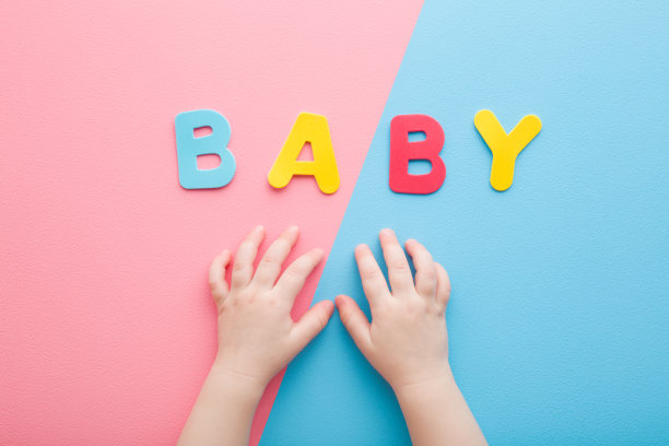 小手和婴儿字创建的彩色字母在浅粉色蓝色的桌子背景。柔和的颜色。特写镜头。视角拍摄。自顶向下的观点。图片下载