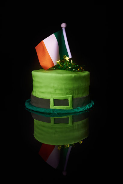 绿色帽子形状的绿色糖霜蛋糕顶部有爱尔兰国旗，庆祝圣帕特里克节。反射在金属黑色的背景上图片下载